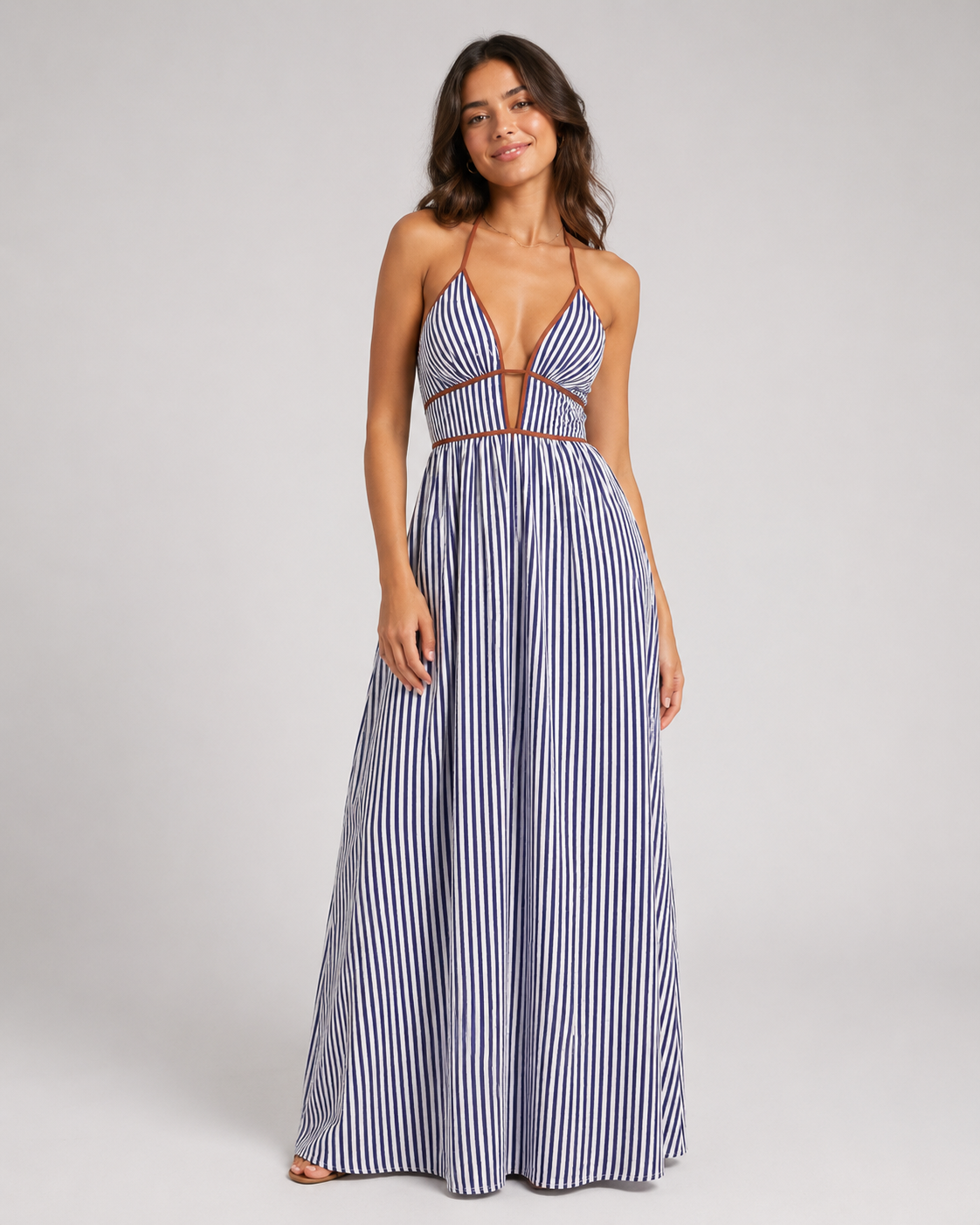 Woman wearing a blue and white striped halter maxi dress with a deep plunging V-neckline and contrasting brown fabric trim.
