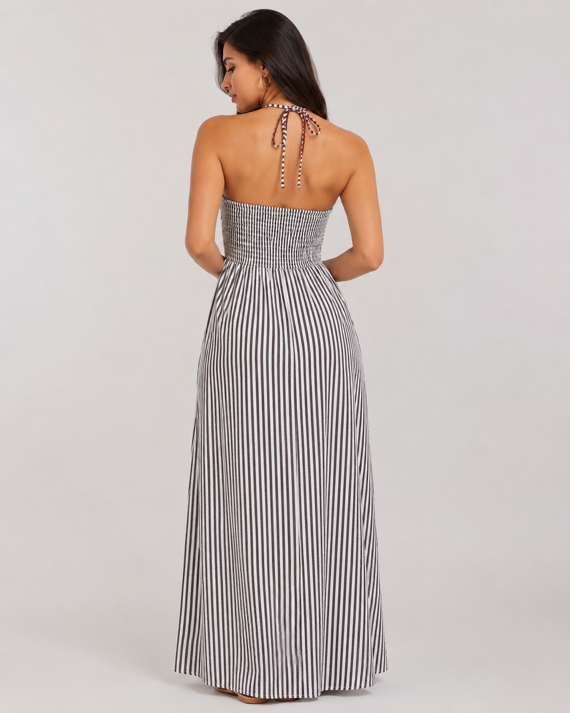 Back view of black and white striped halter maxi dress featuring a smocked elastic bodice and tie-neck closure.